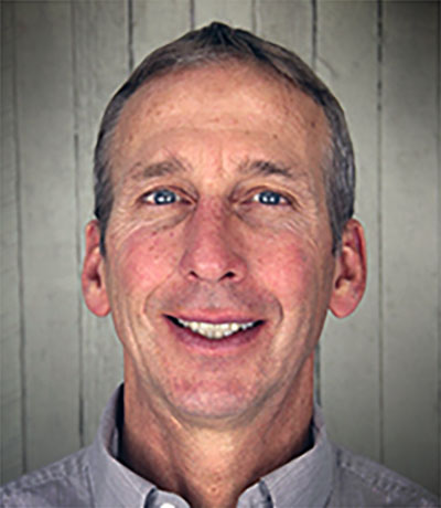 A man with grey hair and blue eyes smiling.