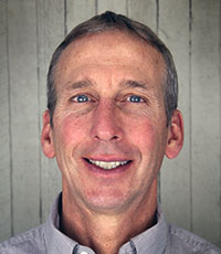 A man with grey hair and blue eyes smiling.